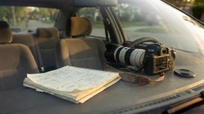 DSLR camera with telephoto lens and handwritten notebook on car dashboard