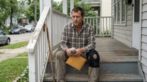 injured man wearing knee brace sitting on porch steps holding envelope and cash