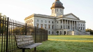 neoclassical state capitol building with domed roof, iron fence, and park bench