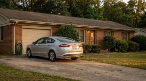 sedan parked in driveway of single-story brick residential home with garage
